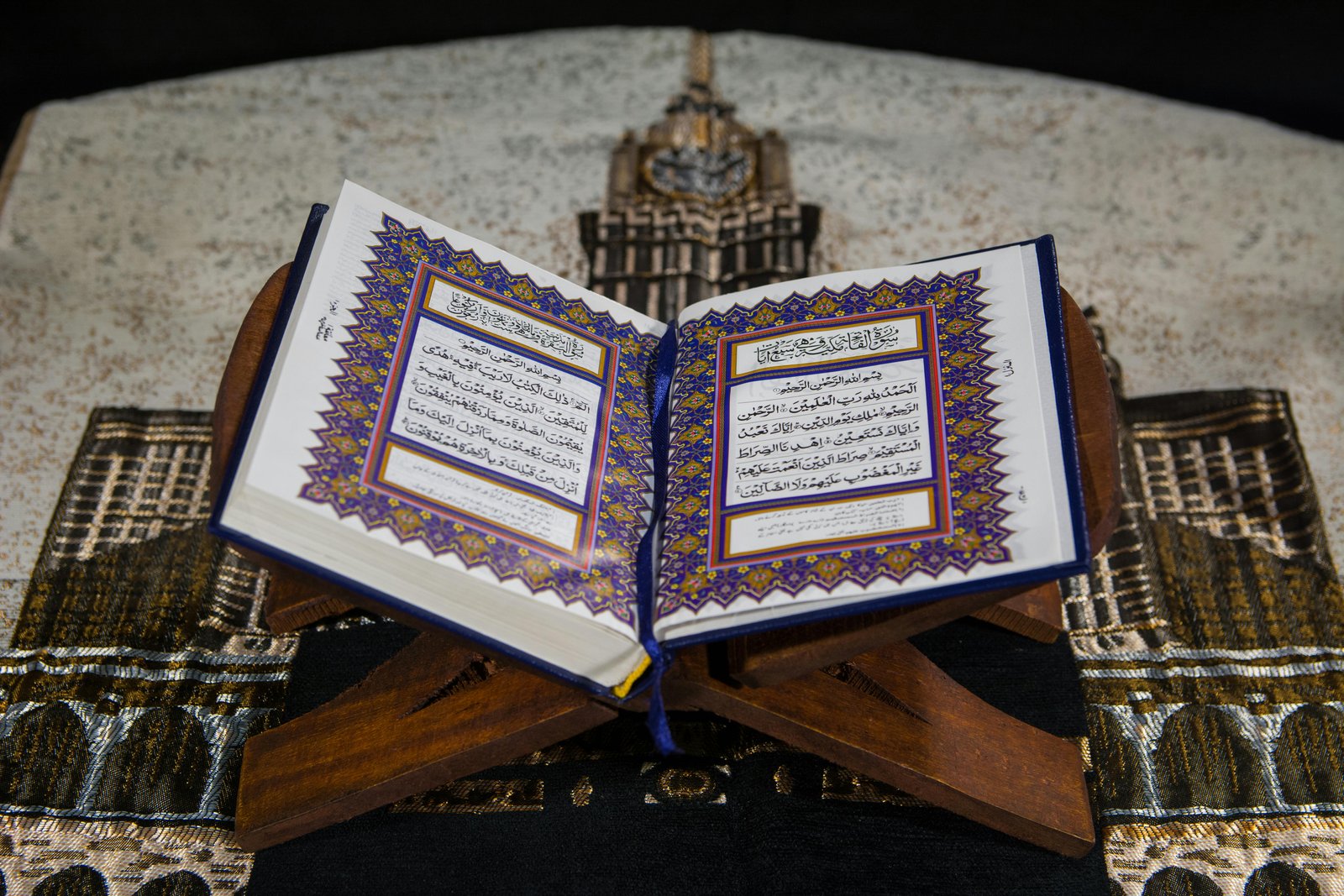 Home An open Quran on a wooden stand atop a prayer rug, emphasizing Islamic faith.